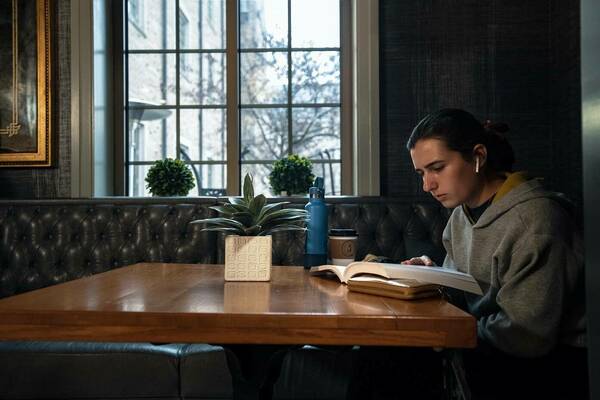 Student with gray sweatshirt with headphones in reading a book at a Morris Inn Lobby Table