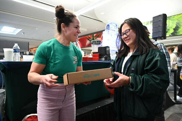 Food Network Chef Stephanie Izard in a green tshirt and light pink jeans handing a box of her sauces to a student who attended her presentation
