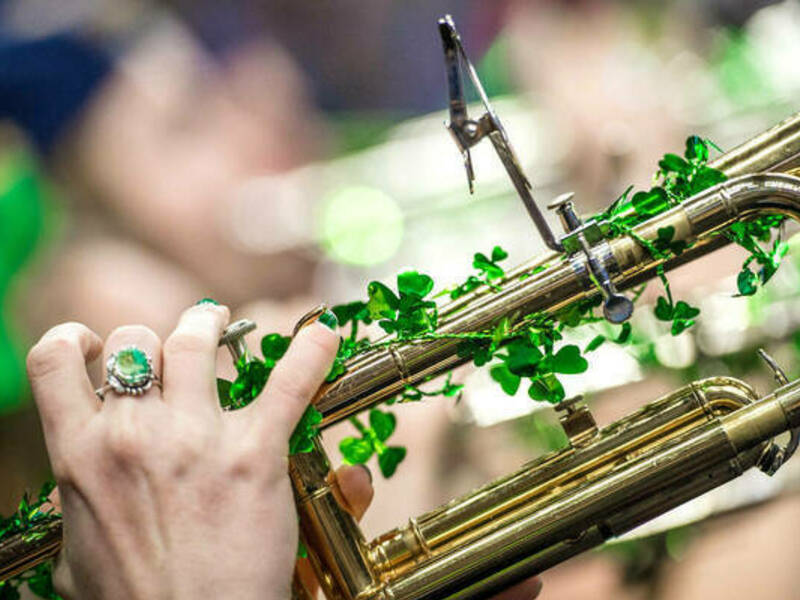 Student's hand playing a trumpet with green shamrocks around it