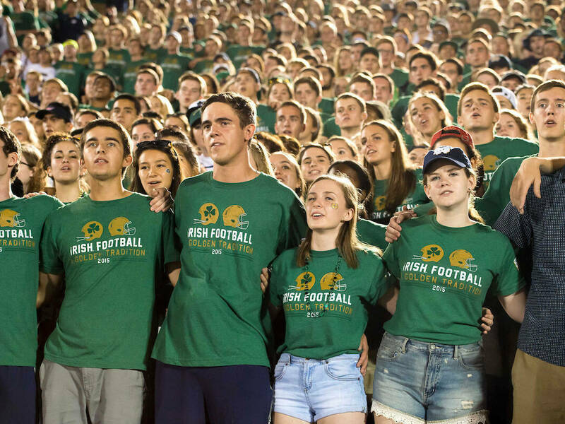 Student section at the end of football game in green shirts in a line for the alma mater
