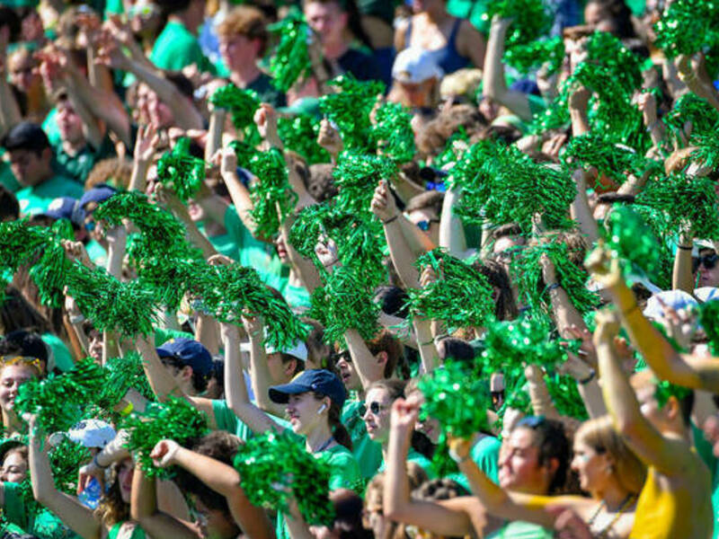 Student section at football game waving green pom poms