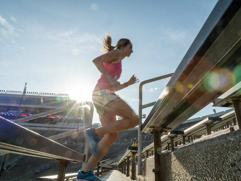 Woman athlete running the stairs of Notre Dame Stadium with the sun shining brightly behind