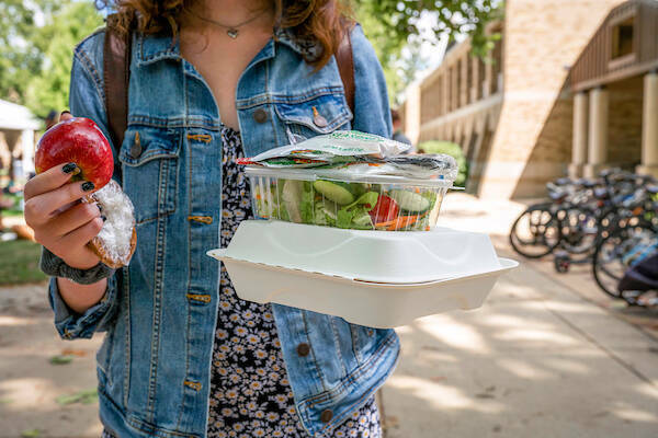 Student holding an apple, salad, and to go box