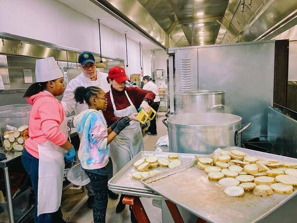 2 chefs helping 2 young kids cook in the kitchen