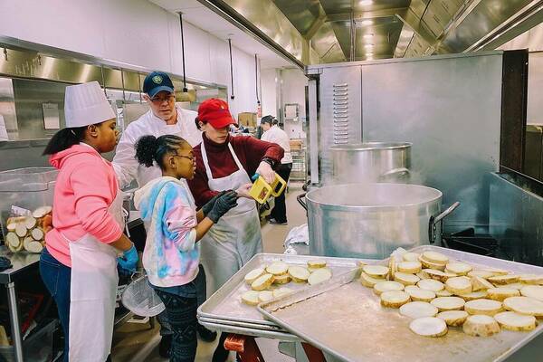 2 chefs helping 2 young kids cook in the kitchen