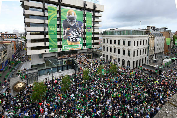 Photo of the Notre Dame band under a Fighting Irish poster that covers a building in Dublin, Ireland