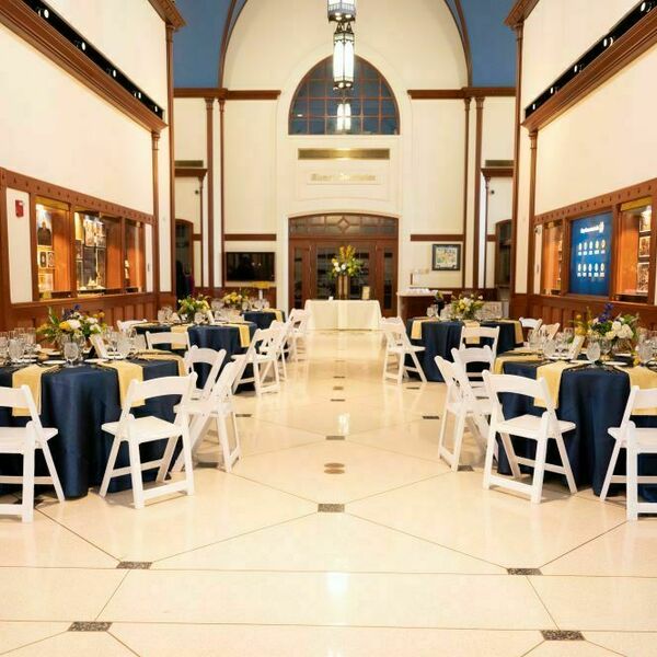 Eck Visitors Center Event Space decorated for a wedding. Decorations include tables with navy blue tablecloths and blue gold touches. White chairs surround the tables.