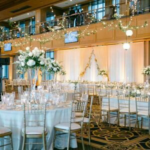 Downes Club event space decorated for a wedding. Greenery and lights hang over tables with white tablecloths, white flowers, and crystal dinnerware.