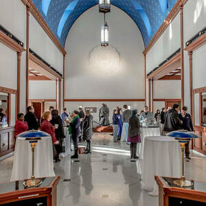 Tables with white tablecloths fill the atrium for an event. People are chatting and mingling with each other.