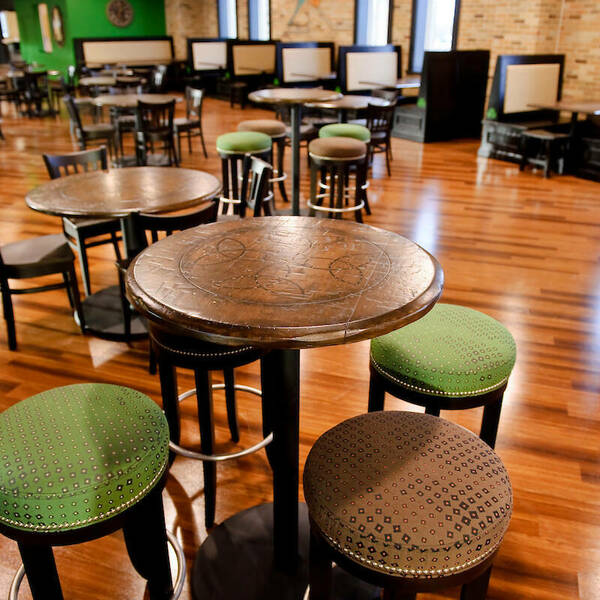 Green and brown stools sit against tall round tables. Shorter tables and booths can be seen in the background.