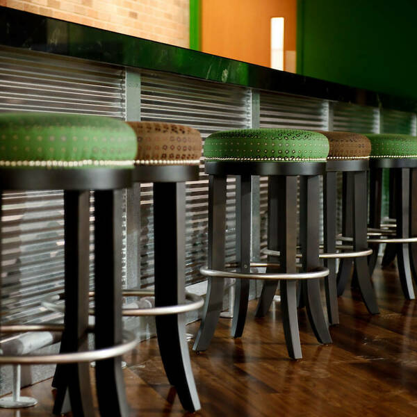 Close up angle of the green and brown barstools sitting against the iron bar.