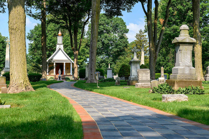 A cobblestone pathway leaded to All Souls Chapel. The chapel is a small A-frame building. Graves line the sides of the path.