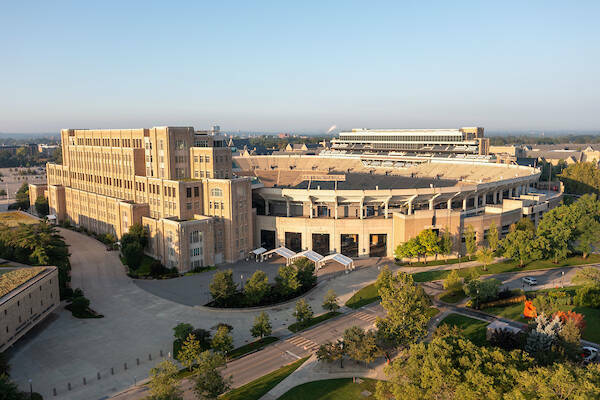 Top view of the Notre Dame Stadium. Blue skies encompass the stadium and full, green trees line the edge of the stadium and surrounding areas.