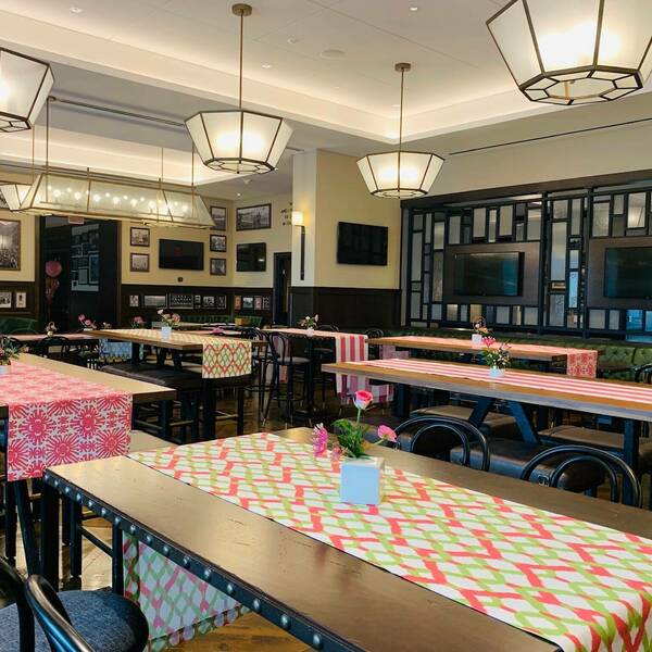 Foley's event space decorated with colorful tablecloths. Pink flowers sit atop each table. Pictures hang on the walls and dark leather green couches line the sides of the rooms.