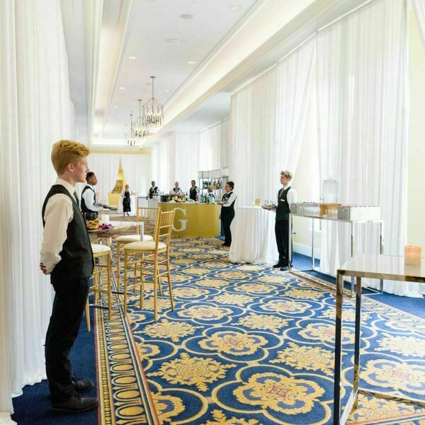 White curtains line the outside hall of the Smith Ballroom. Tables and a bar fill the sides of the hall and people serve appetizers.