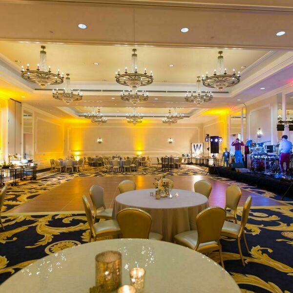 Smith Ballroom at Morris Inn decorated in yellow and white for a wedding. A large stage with instruments and performers sits at the front behind a large wooden dance floor. Circular tables with flowers and candles line the sides of the dance floor.