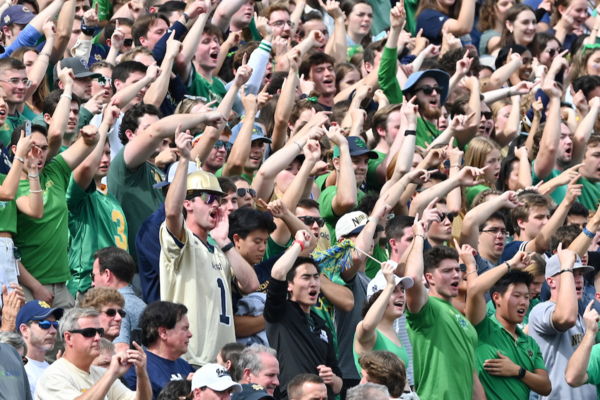 Students and guests in green and gold Notre Dame gear cheering on the football team.