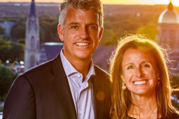 A well-dressed couple posing for a photo with the campus of the University of Notre Dame in the background.